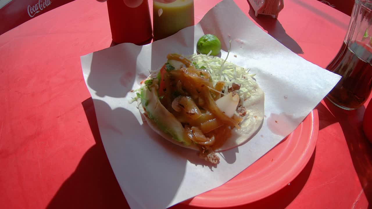 Maskuline hænder presser lime over en street taco med svinekød, avocado, salat og løg.