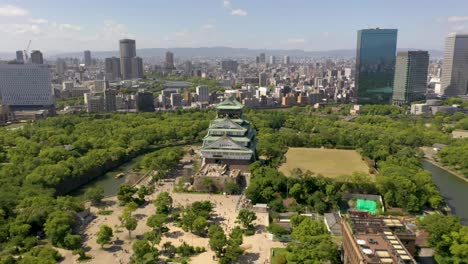 Aerial-of-historic-landmark-Osaka-Castle-with-park,-moat,-skyscraper,-and-city-in-Osaka,-Japan