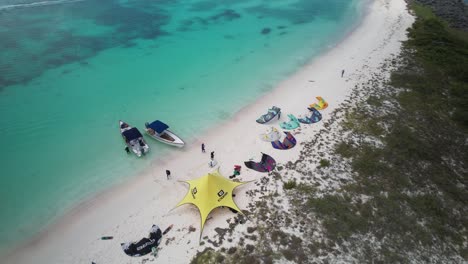 kitesurfing gear laid out on a remote sandy beach by turquoise waters, aerial view