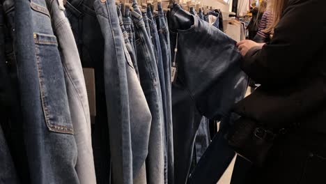 the woman looks through and touches the pants on the hangers in the clothing store. pants offer in shops