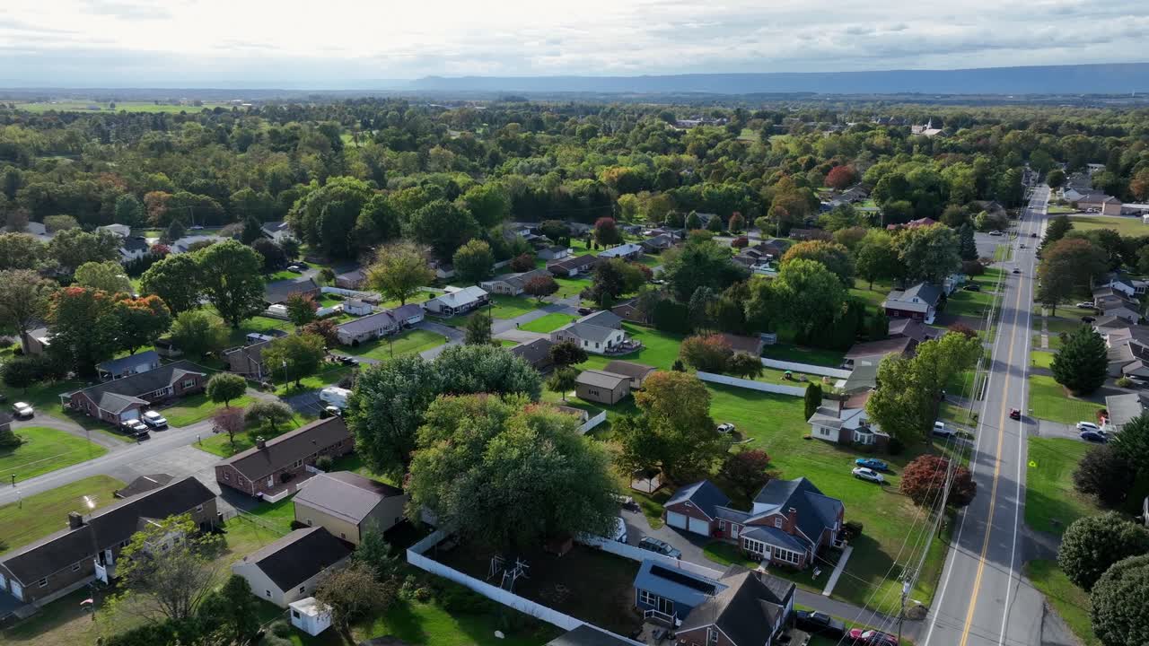 Panoramica aerea di un quartiere americano con aree verdi e auto che percorrono la strada principale. Campo lungo. Sorvolo. Case unifamiliari e alberi colorati in autunno.