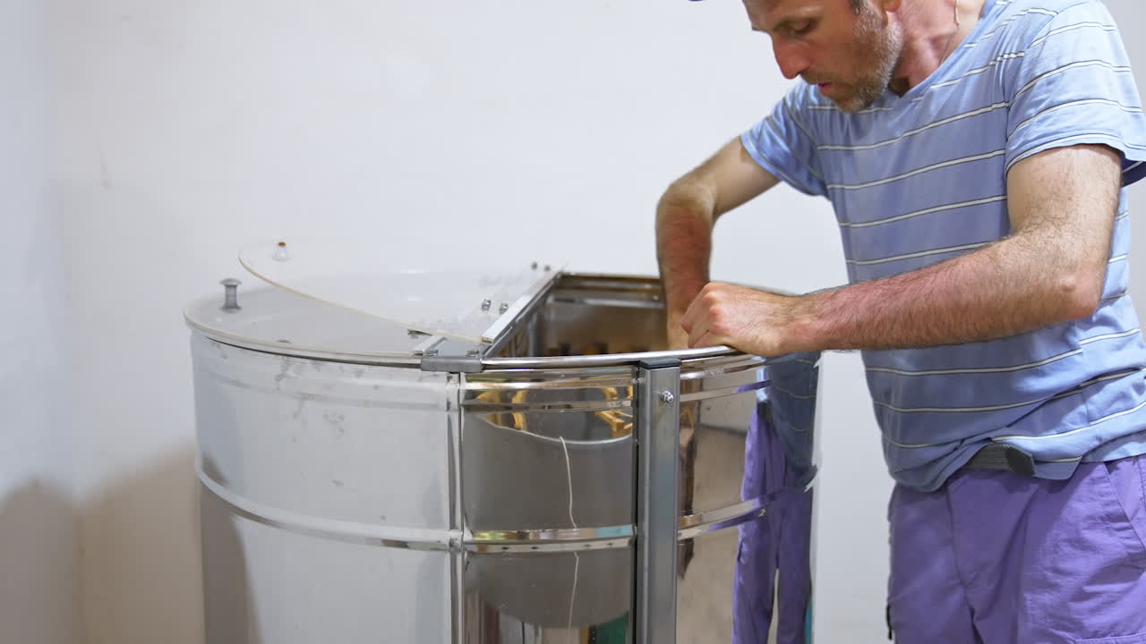 Bee farmer puts the frames into a metal barrel to get honey. Man carefully places the honeycombs into special apparatus.