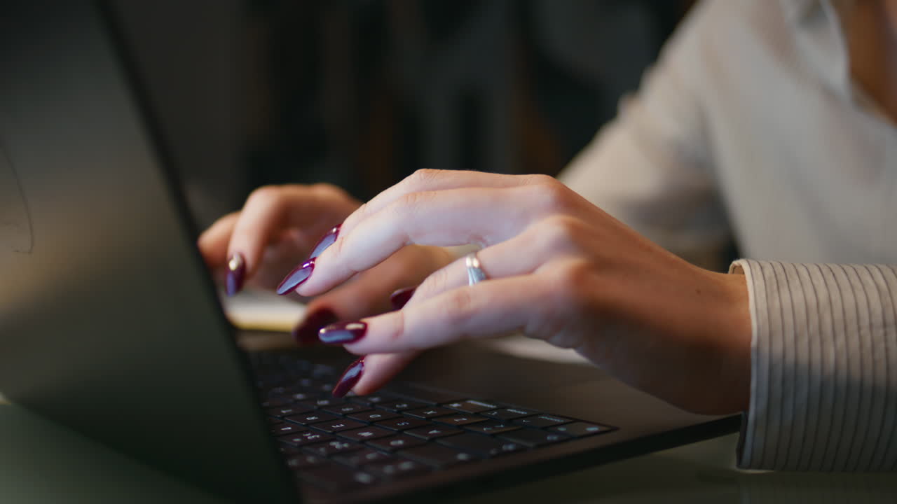 Primo piano di una ragazza che lavora fino a tardi digitando sulla tastiera di un laptop in ufficio di sera.