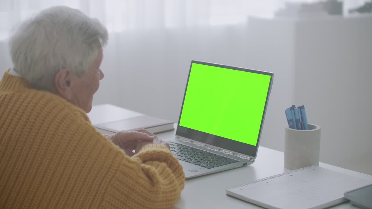 una mujer mayor mira un monitor con una pantalla verde y habla a través de un enlace de video con su nieta o hija o un médico. ayuda de video para los ancianos. la abuela usa una computadora portátil