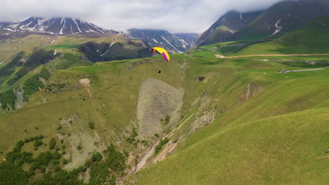 wide rotating drone shot of paraglider flying in the caucasus mountains in gudauri georgia