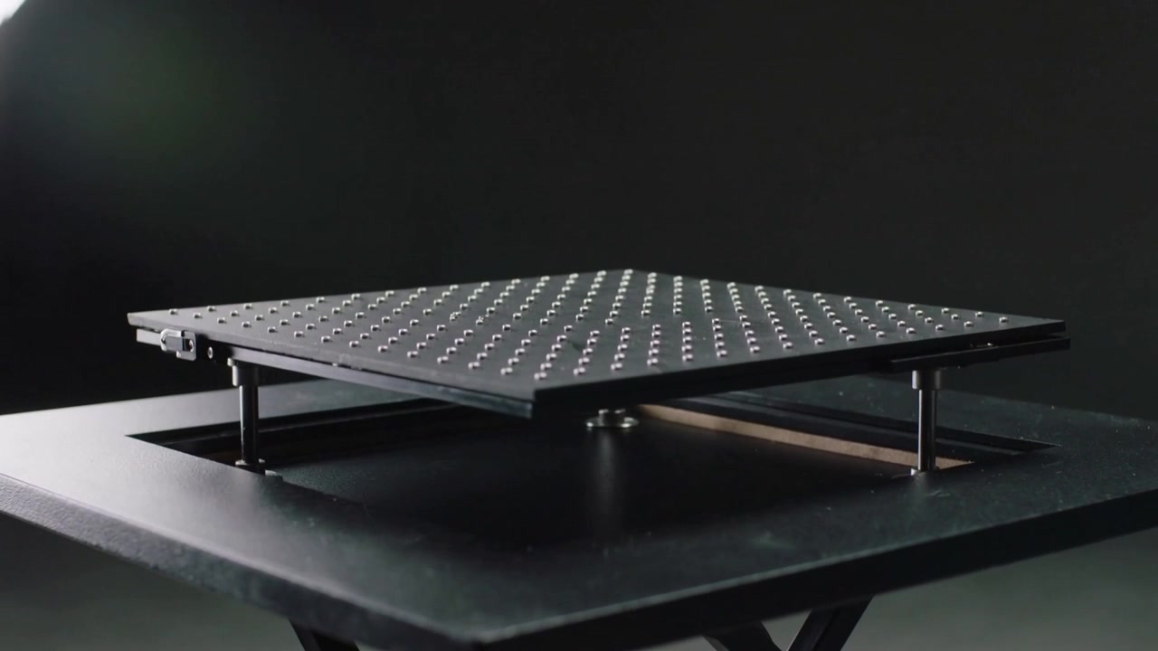 Releasing left latch, perforated plate with studs rising from tabletop in studio, revealing posts