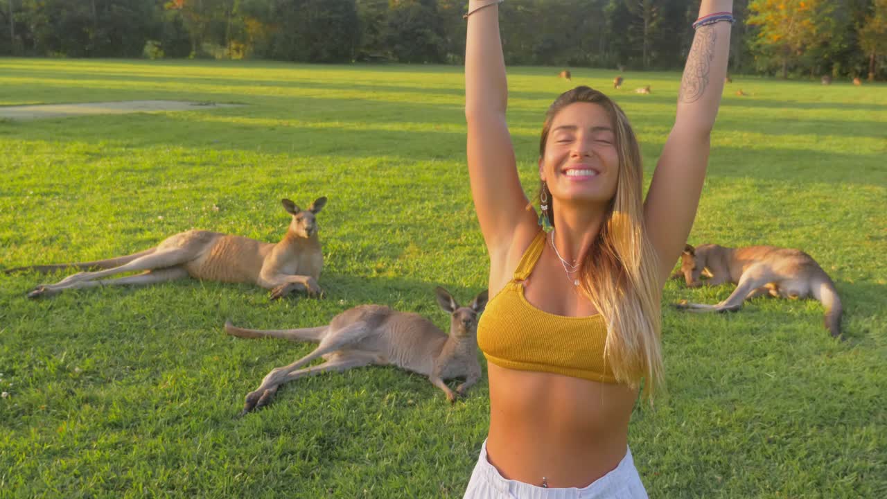Bella ragazza in bralette, con le mani alzate e canguri grigi orientali che riposano sullo sfondo - Gold Coast, QLD, Australia