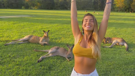 hermosa chica en bralette levantó ambas manos con canguros grises orientales descansando en el fondo - costa dorada, qld, australia