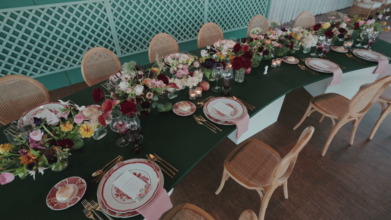 Long dining table decorated with colorful flowers plates glassware and cutlery arranged for wedding reception indoors