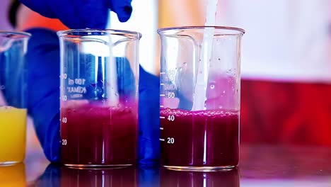 gloved lab technician stirs color changing red and yellow liquids using plastic spoon
