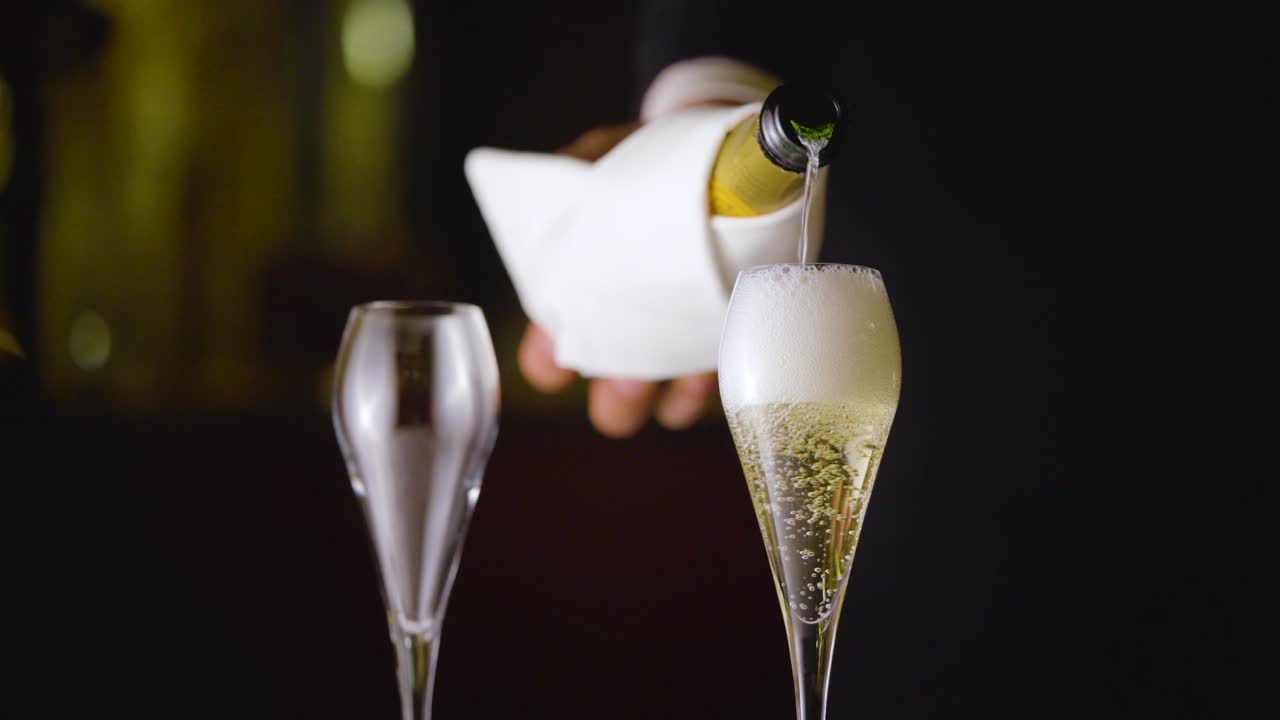 A waiter is filling up the glass with luxury champagne bubbles from a white wrapped bottle. Veuve Clicquot