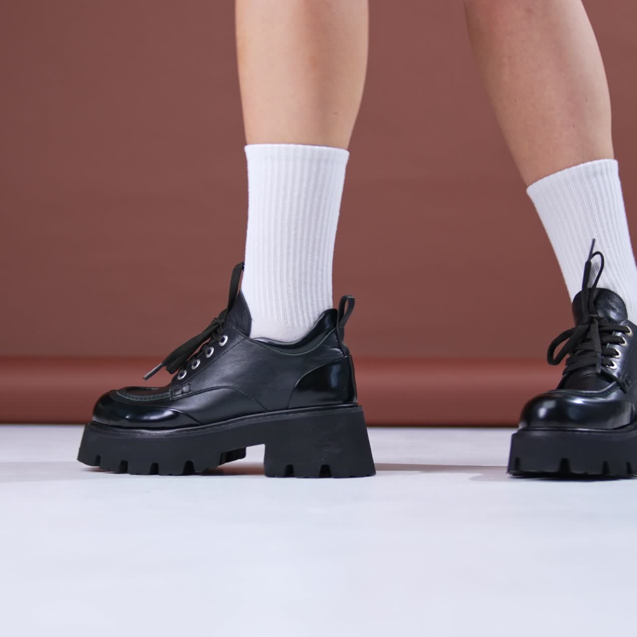 Black leather autumn shoes on massive tractor soles. Model in white socks demonstrates her modern stylish footwear dancing in front of camera. Close up