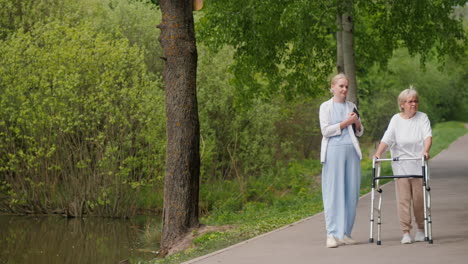 elderly woman with walking aid being supported by a caregiver in a park.