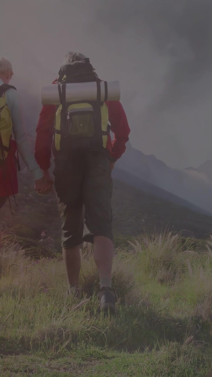 Video vertikal: Pendaki memeriksa peta untuk navigasi dan mendaki punggung bukit, kabut merah menyapu kaki