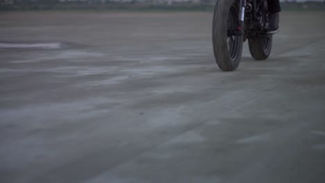 primer plano del paseo de un motociclista en una bicicleta deportiva negra con el faro delantero encendido por un terreno arenoso