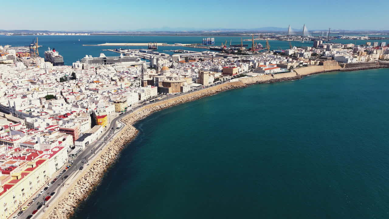 Panorama aereo da drone della costa di Cadice e del paesaggio urbano storico che si snoda lungo l'Oceano Atlantico, con edifici bianchi del centro storico e lungomare in una luminosa giornata di sole in Andalusia, Spagna. Toni scuri