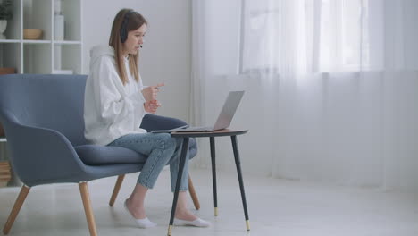 Young-woman-wears-headset-conference-calling-on-laptop-talks-with-online-teacher-studying-working-from-home.-Lady-student-e-learning-using-computer-webcam-chat-makes-notes.-Distance-education-concept