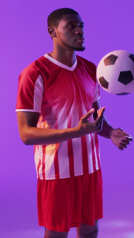 video vertical de un jugador de fútbol masculino afroamericano con fútbol sobre iluminación rosada