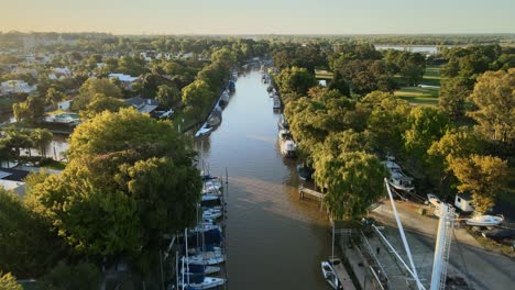 Aerial-following-a-river-path-with-several-boats-docked-and-at-sides-some-houses