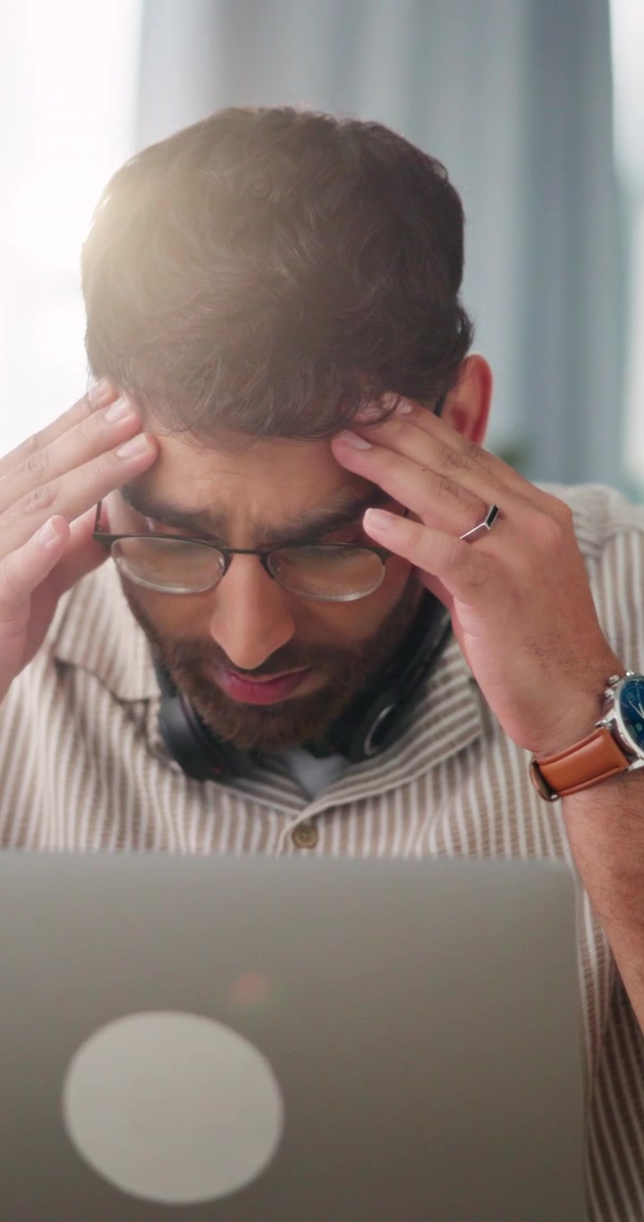 Uomo stressato che lavora al laptop nel suo ufficio domestico.