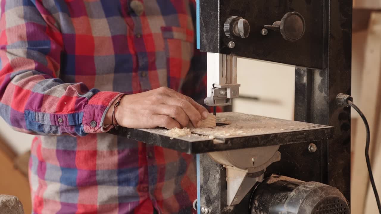 Primo piano di un falegname che lavora con una sega a nastro tagliando il legno in officina. Processo dettagliato di lavorazione del legno con attenzione all'artigianato, agli attrezzi e all'abilità manuale, ideale per temi fai-da-te e artigianali.