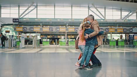 happy father meeting his arriving family from vacation travel , embracing with wife and children at airport building