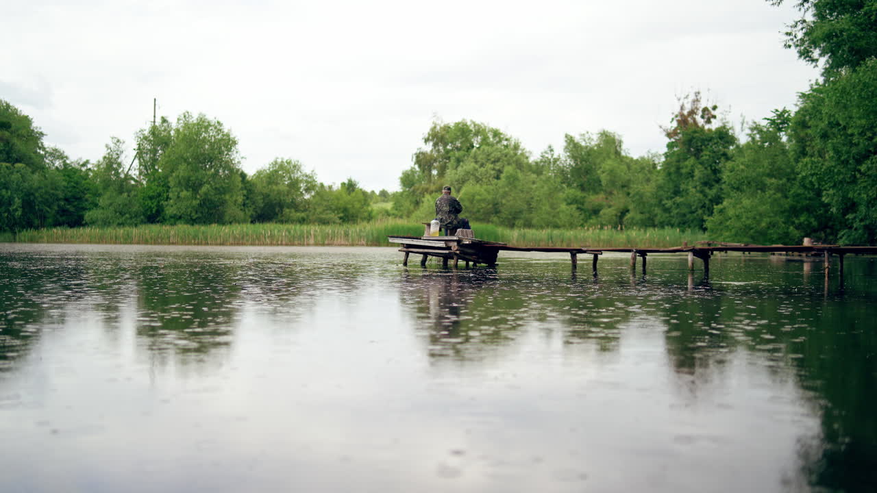 Fisherman catching fish on lake. Rear view of man sits on the pier and catches fish in the lake