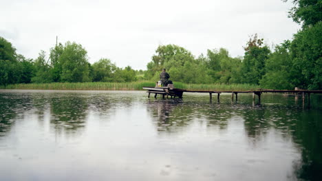 fisherman catching fish on lake. rear view of man sits on the pier and catches fish in the lake