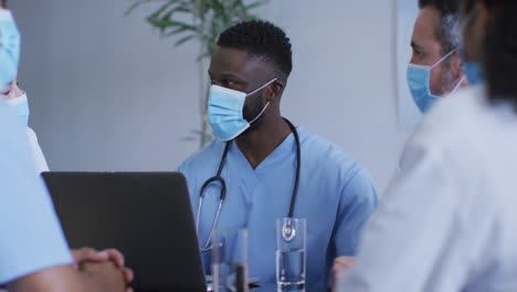 African-american-male-doctor-and-diverse-hospital-colleagues-wearing-face-masks-talking-at-meeting