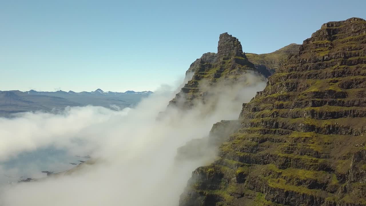 antena elevándose sobre la verde y empinada cumbre de una colina, nubes que cubren las montañas en el fondo, en la pequeña ciudad de djúpivogur cerca de los fiordos de islandia durante el día