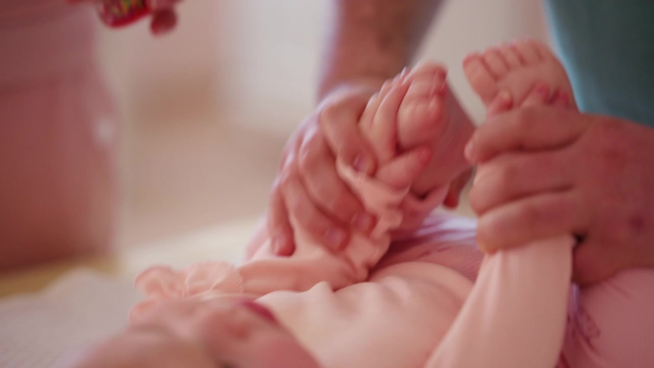 Um bebê deita-se confortavelmente enquanto observa um brinquedo colorido e faz exercícios de mobilidade com um cuidador.