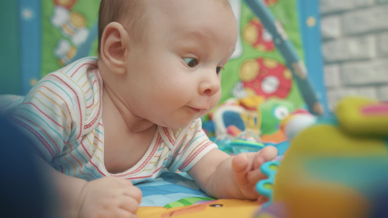 다채로운 장난감과 함께 아기 아기 소년. 장난감과 함께 다채로운 매트에 누워있는 즐거운 아이