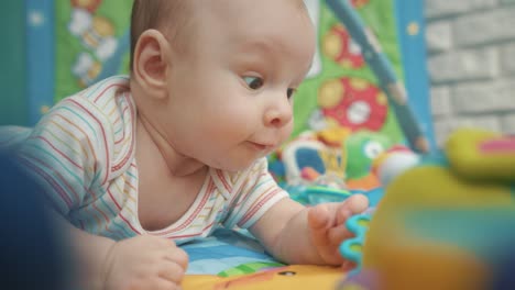 infant baby boy with colorful toys. cheerful kid lying on colorful mat with toys