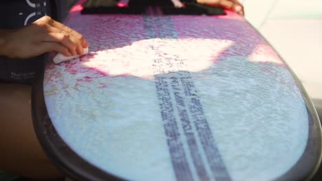 female hand waxing pink and white wake surf surfboard in preparation for water sports