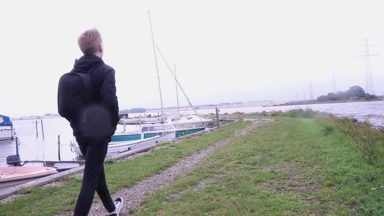 Guy with backpack walking away from camera at small harbor