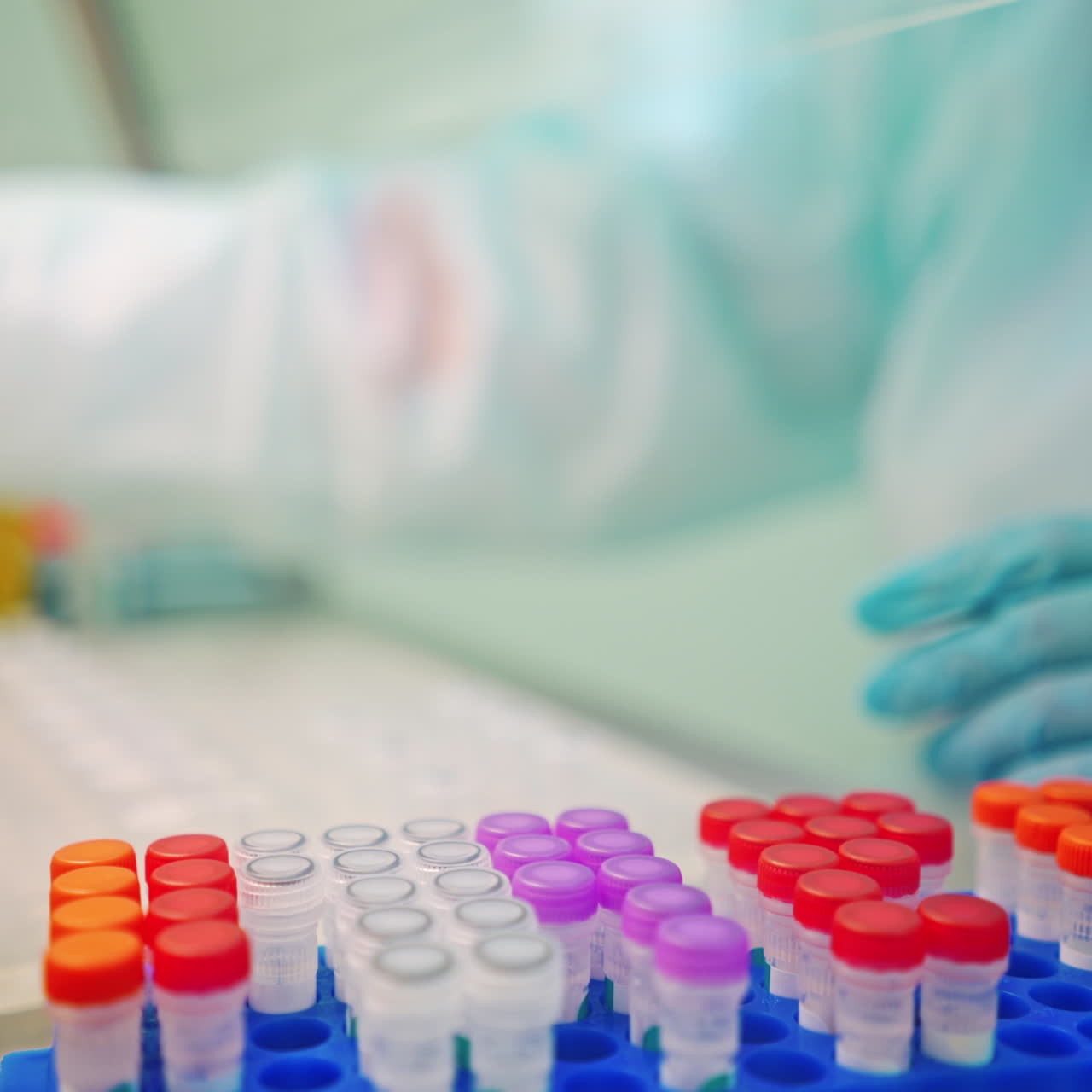 Laboratory worker in protective gloves is checking test tubes. Vials with liquid with colorful covers on a support in a laboratory.