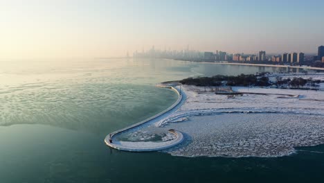 aerial view over ice and the montrose harbor beacon and pier, foggy, winter sunrise in chicago, usa