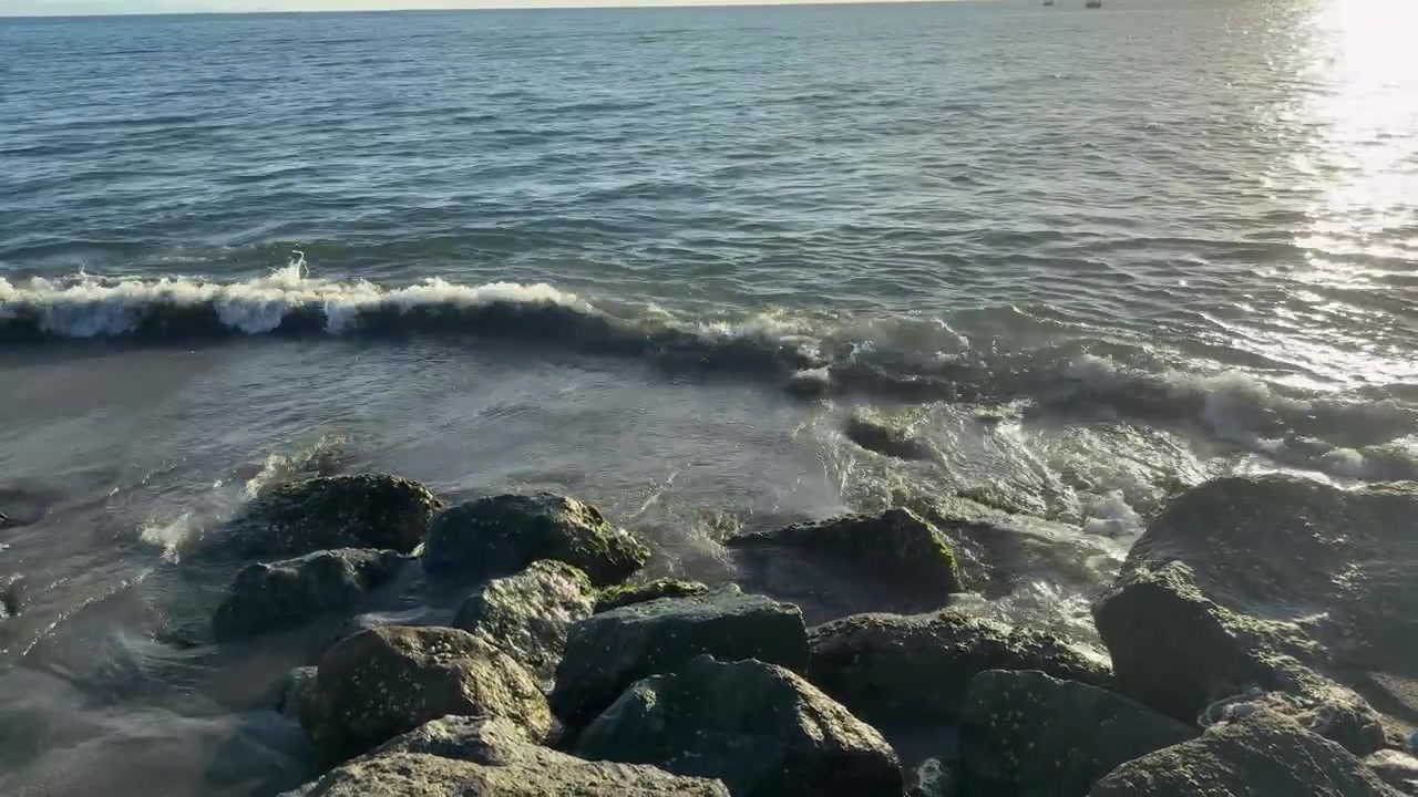 Onde serene dell'oceano che si infrangono su una spiaggia rocciosa con riflessi di sole