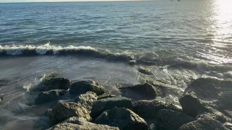 Onde serene dell'oceano che si infrangono su una spiaggia rocciosa con riflessi di sole