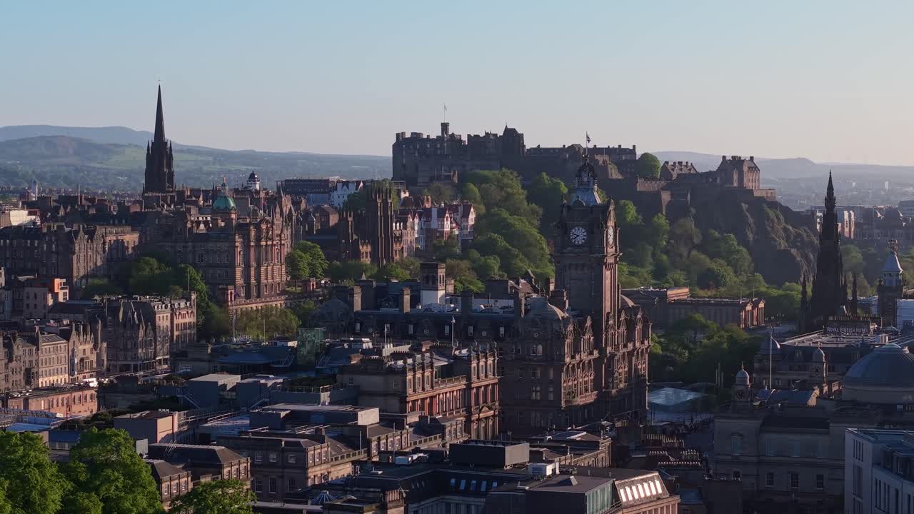 Drone footage capturing a sunny morning over Edinburgh’s old city and iconic castle, showcasing historic rooftops and the vibrant urban landscape under clear blue skies