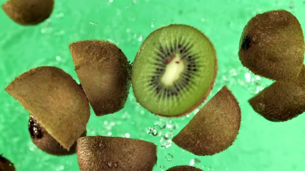 Mitades de kiwi fresco flotando en agua con salpicaduras sobre fondo verde.