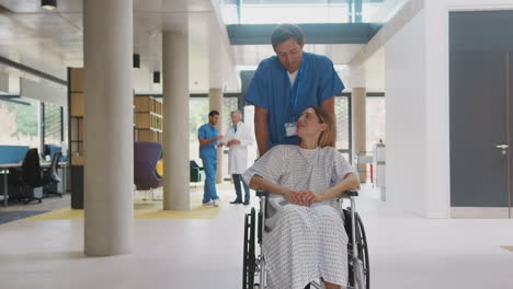 male nurse wearing scrubs pushing female patient in wheelchair through hospital building