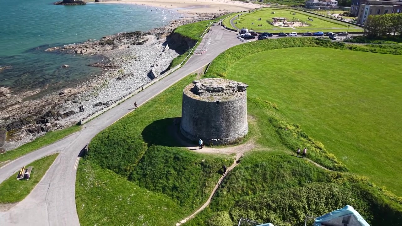 Órbita panorámica de dron de la Torre Martello y la costa de Balbriggan bajo el sol dorado de verano