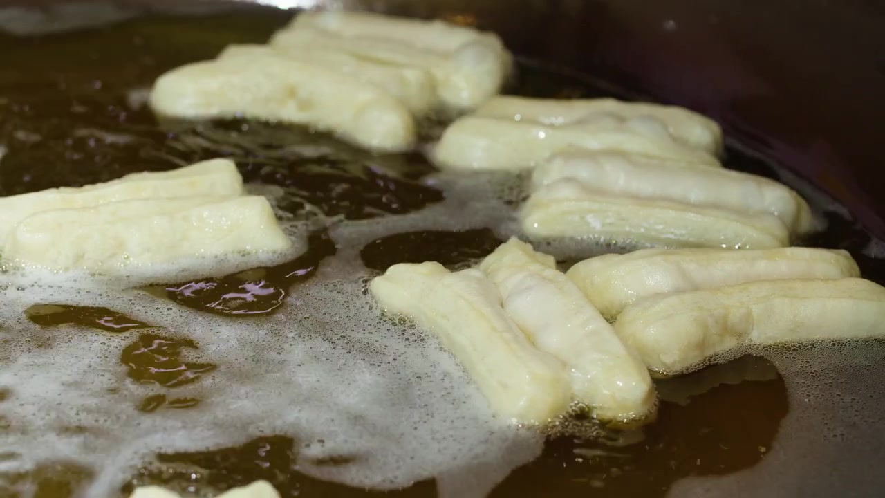 Close-up of youtiao dough frying in bubbling oil during breakfast preparation at a market.