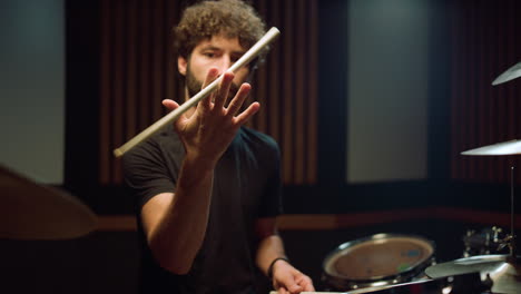 Musician-twirling-drumstick-in-studio.-Rock-drummer-sitting-in-concert-hall.