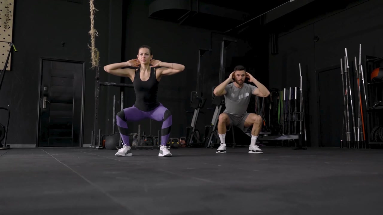 Uomo e Donna che Eseguono Squat in una Palestra Moderna