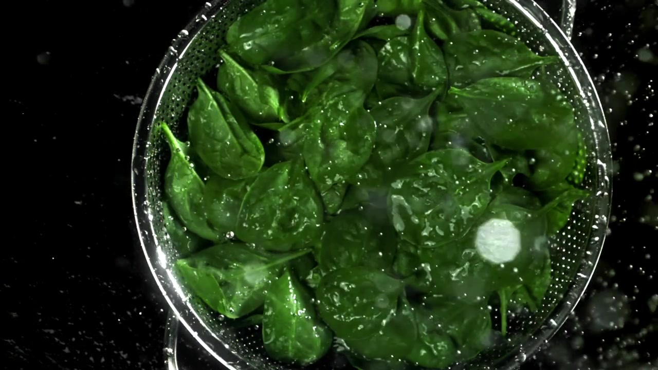 Lavaggio di foglie fresche di spinaci verdi in uno scolapasta