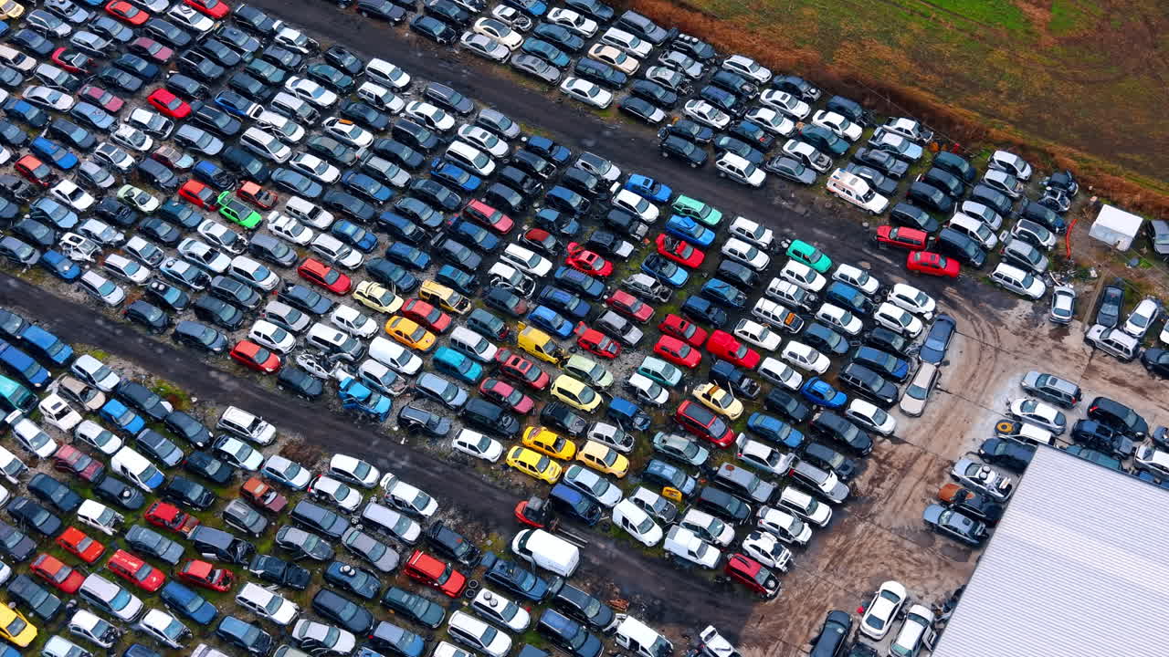 Topbillede af bilgenbrugscenter med gaffeltruck i drift. Luftfoto med drone af en skrotplads med rækker af biler og en lille maskine, der flytter et køretøj i midten.