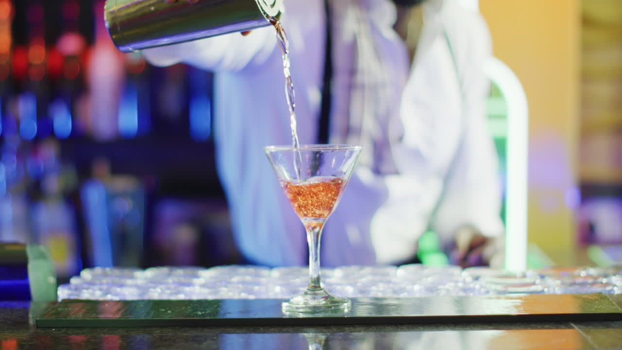 Video of midsection of african american barman poring pink cocktail at the bar