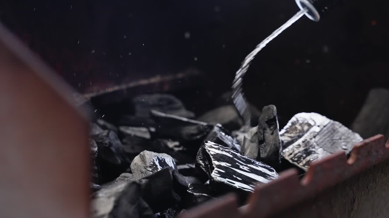 Hand pours lighter fluid onto coals in grill during backyard barbecue setup